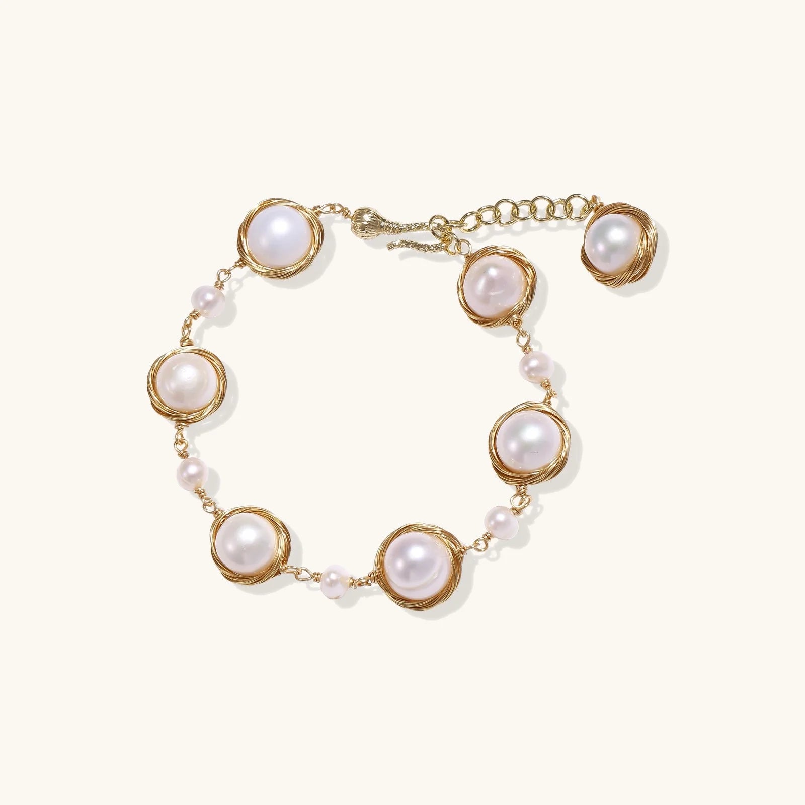 Gold wire-wrapped freshwater pearl bracelet with alternating pearl sizes on cream background, adjustable length