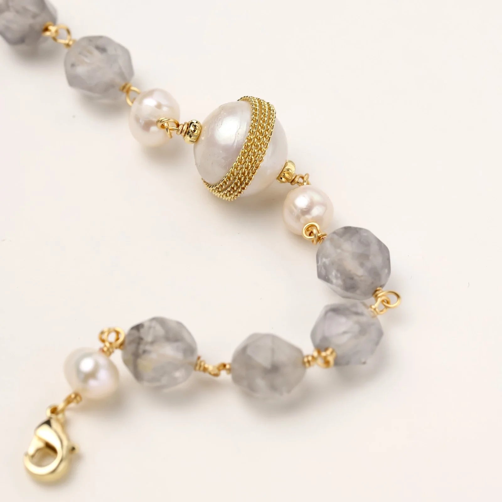Bracelet with cloudy quartz beads, freshwater pearls, and gold-wrapped baroque pearl centerpiece on white background.