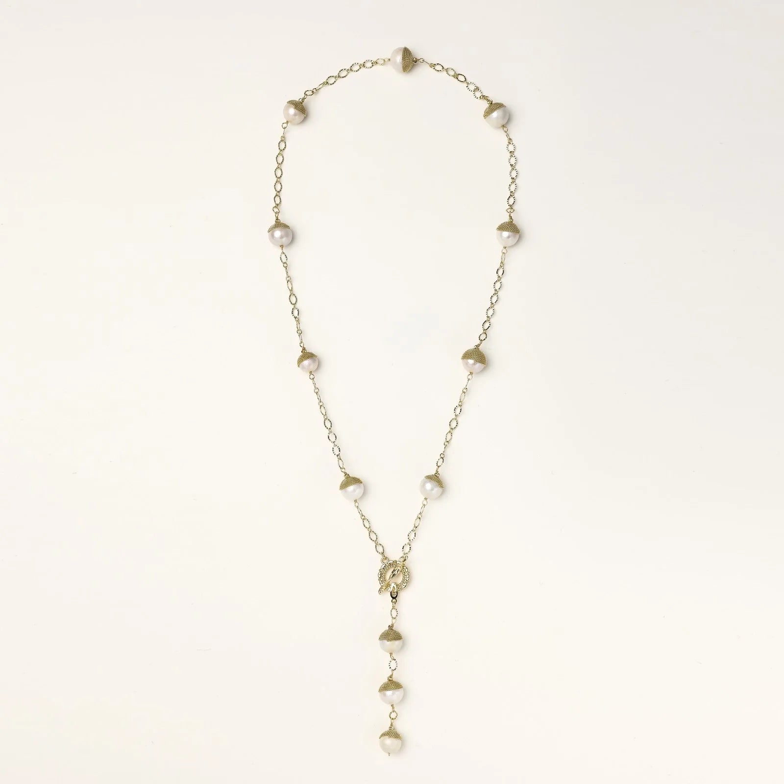 Gold-plated lariat necklace with baroque pearls and textured caps on cream background, showing adjustable Y-shaped design.