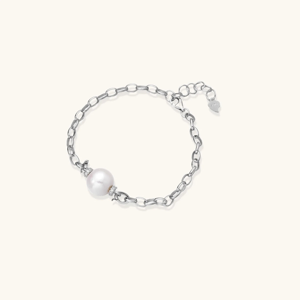 Rhodium-plated silver chain bracelet with single white freshwater pearl and heart charm clasp on cream background