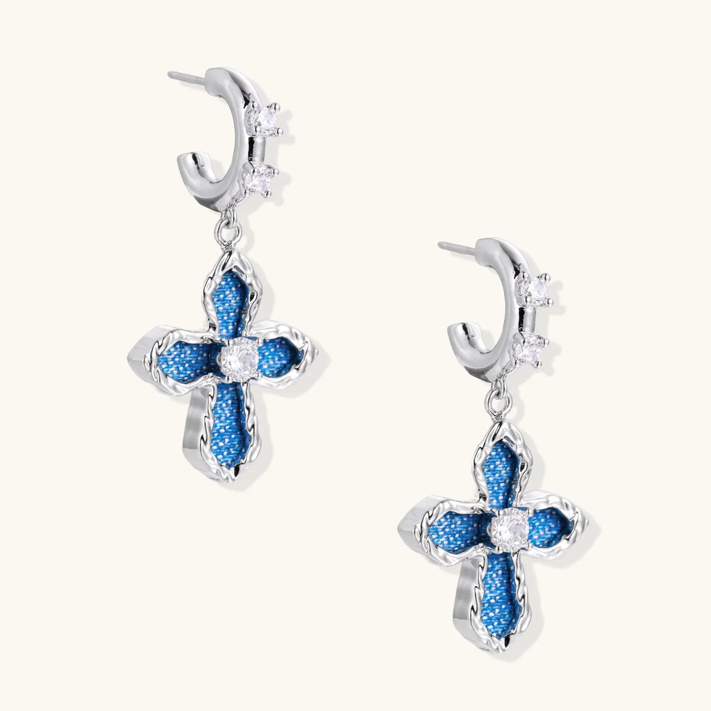 Silver hoops with denim-inlaid cross charms and clear crystals on beige background