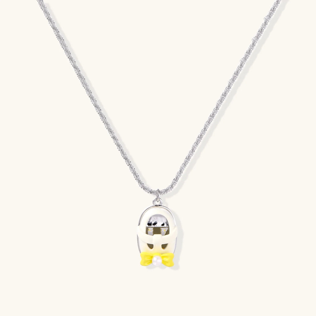 Chrome egg-shaped pendant with kawaii face, yellow bow, and pearl detail on silver chain against white background