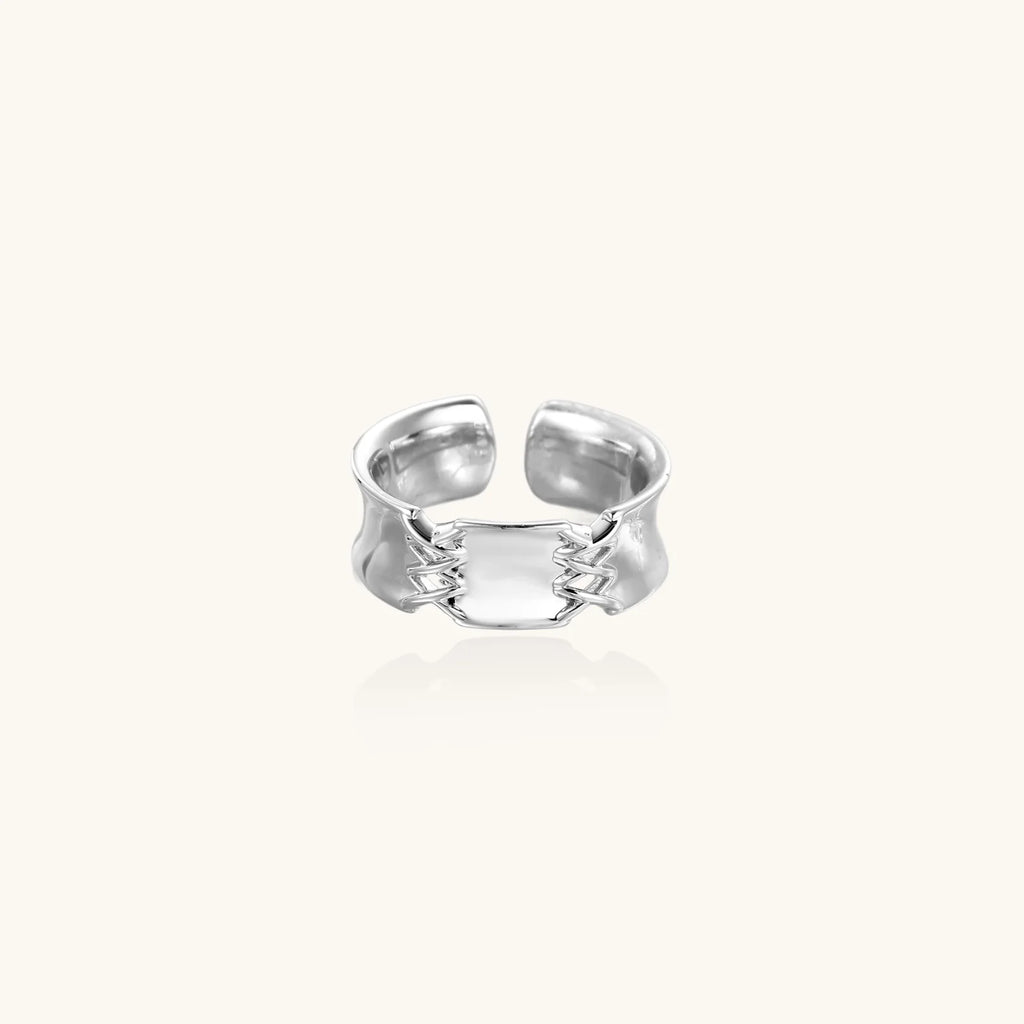 Adjustable silver-toned ring with sculptural stitch design across polished white gold-plated brass band