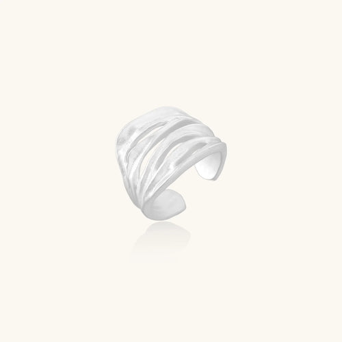 Wide sterling silver cuff ring with flowing wave patterns creating dimensional texture against cream background