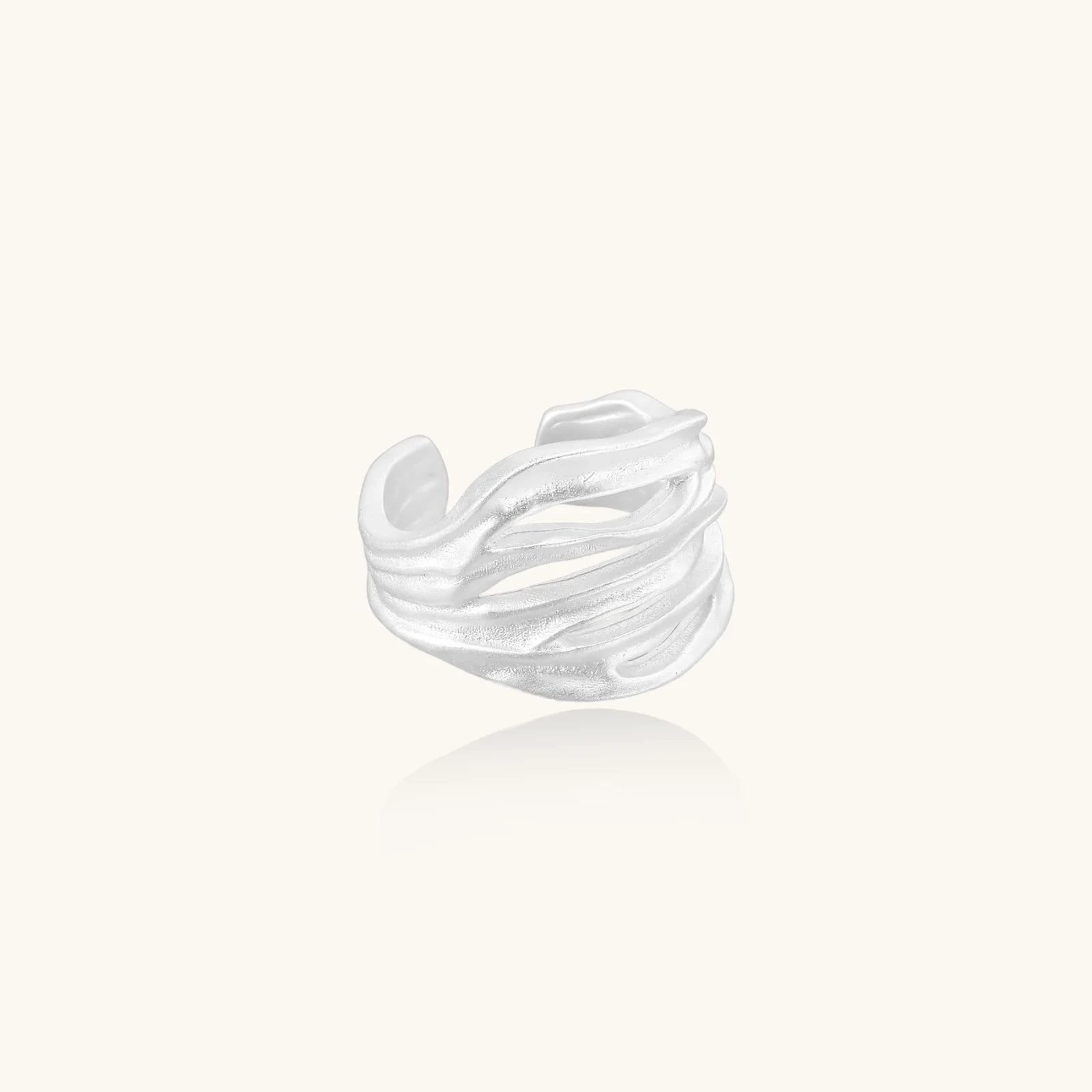 Wide sterling silver cuff ring with flowing wave patterns creating dimensional texture against cream background