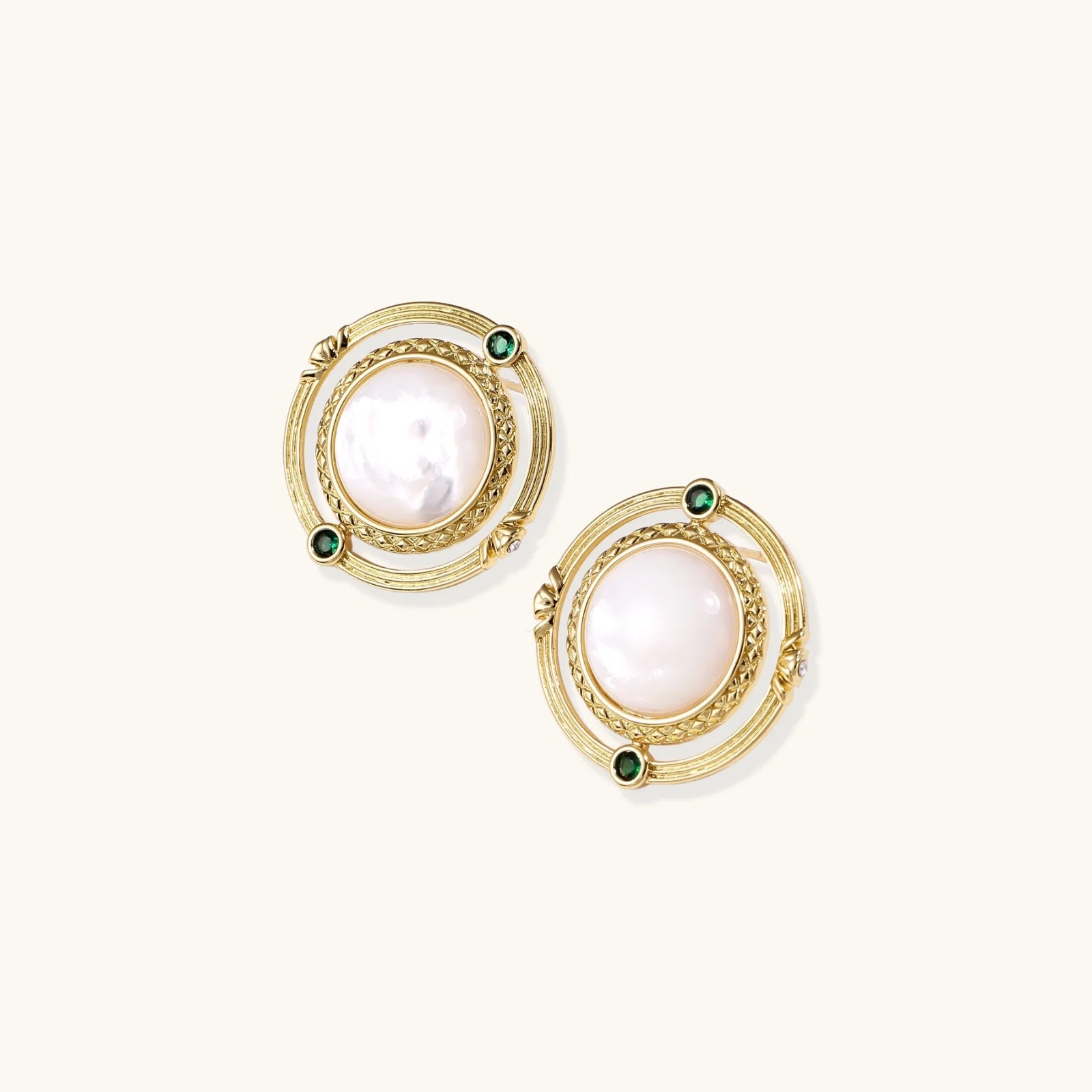 Circular gold stud earrings with iridescent mother-of-pearl center and green zirconia accents on cream background.