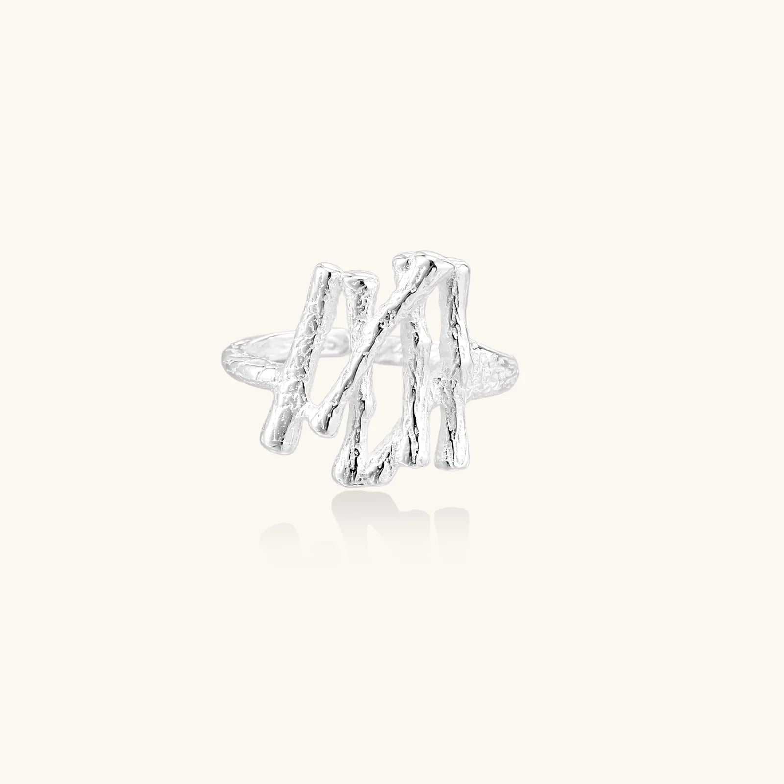 Sculptural sterling silver ring with organic branch design and textured surfaces on cream background