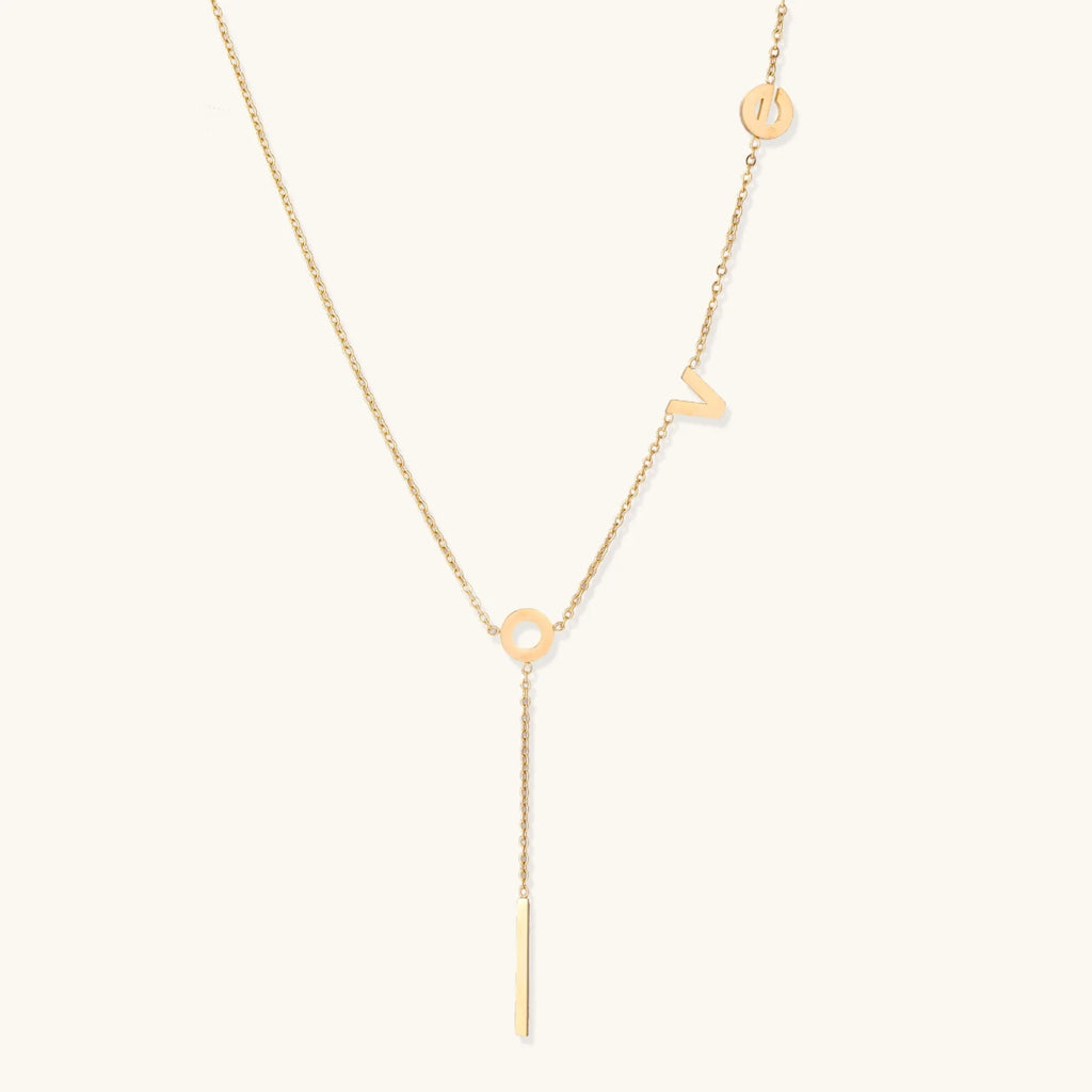 Gold Y-shaped necklace with L-O-V-E letter charms and vertical bar pendant on delicate chain against cream background