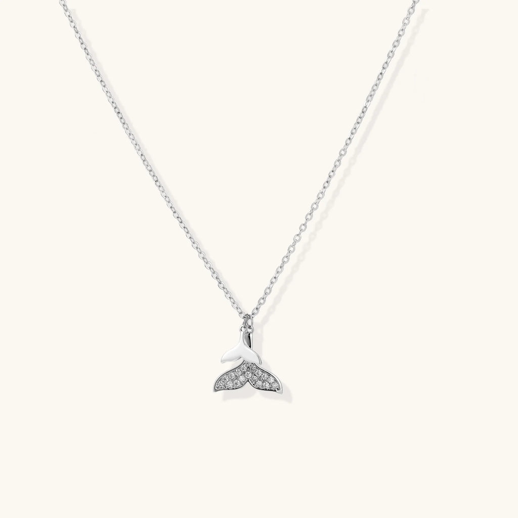 Delicate white gold plated whale tail pendant with pavé crystals on silver chain against cream background.