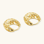 Close-up of small gold-plated hoop earrings with intricate honeycomb cutout pattern on cream background.