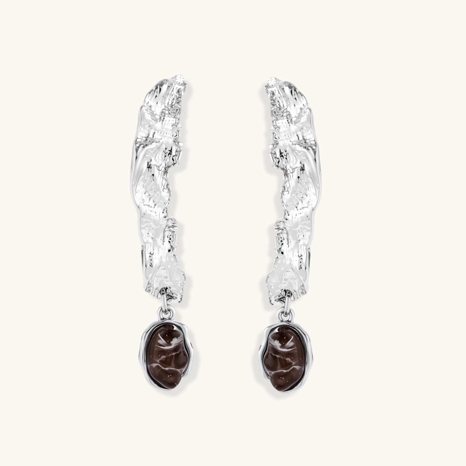 Silver-toned twisted metal earrings with dark brown oval resin stones dangling from sculptural posts on white background.