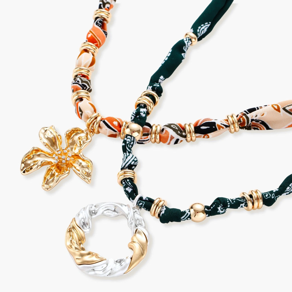 Adjustable necklace with black paisley fabric cord, gold metal spacers, and clear twisted pendant on cream background
