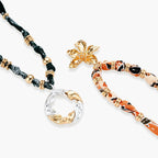 Adjustable necklace with black paisley fabric cord, gold metal spacers, and clear twisted pendant on cream background