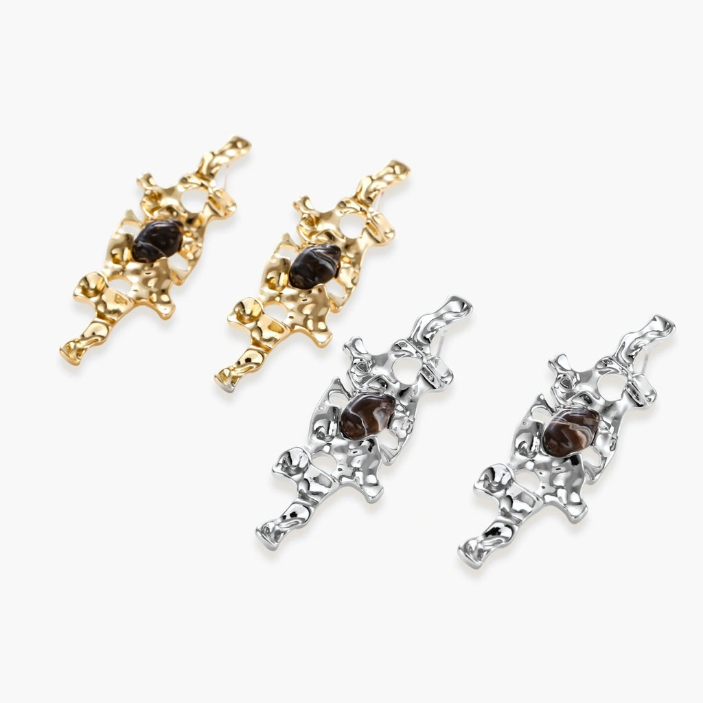 Gold-toned abstract dangle earrings with flowing cutout design and dark resin center accents on white background.